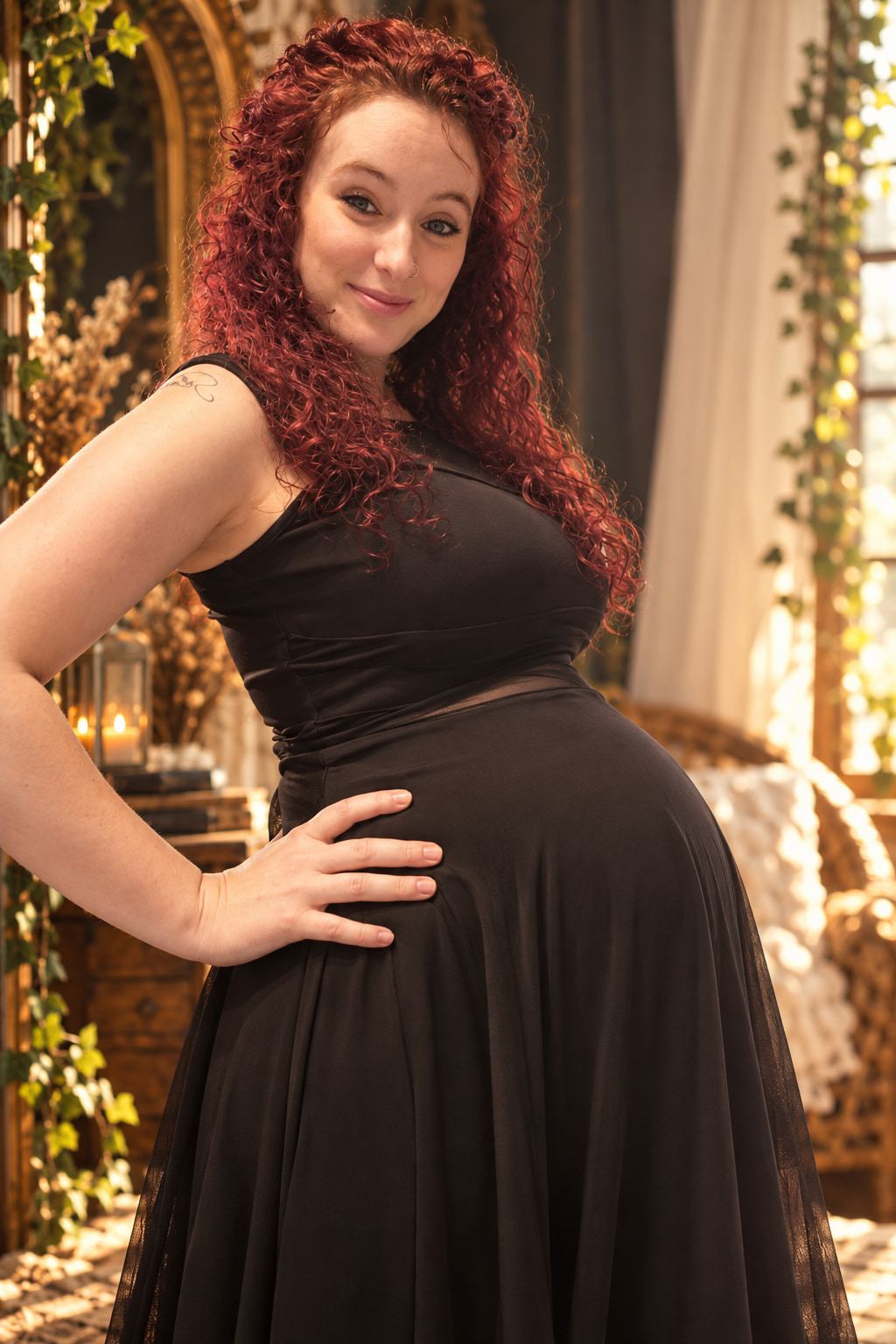 Amanda, pregnant, in a black dress with one hand on her belly, smiling in a sunlit room.